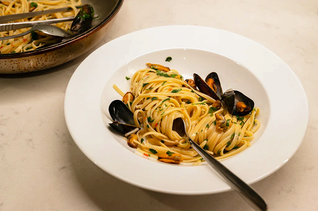 En djup tallrik med linguine eller spagetti vänd med blåmusslor, hackad persilja och chili