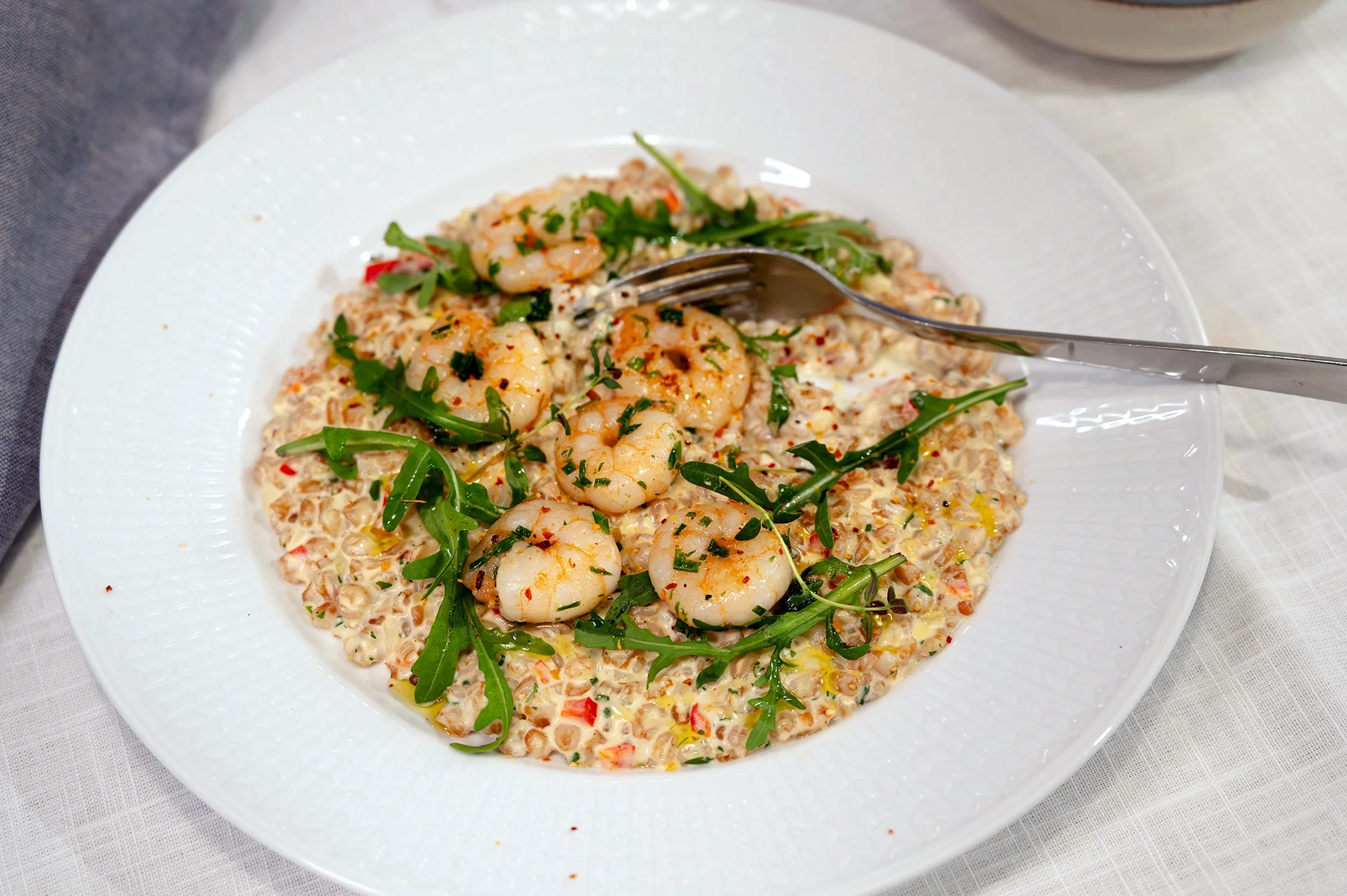 Tallrik med krämigt matvete (grynotto) toppat med stekta vannameiräkor, rucola, örter och chiliflakes