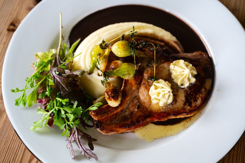 Grillad fläskkotlett med ben – serveras med potatispuré, rödvinssås och vitlökssmör.