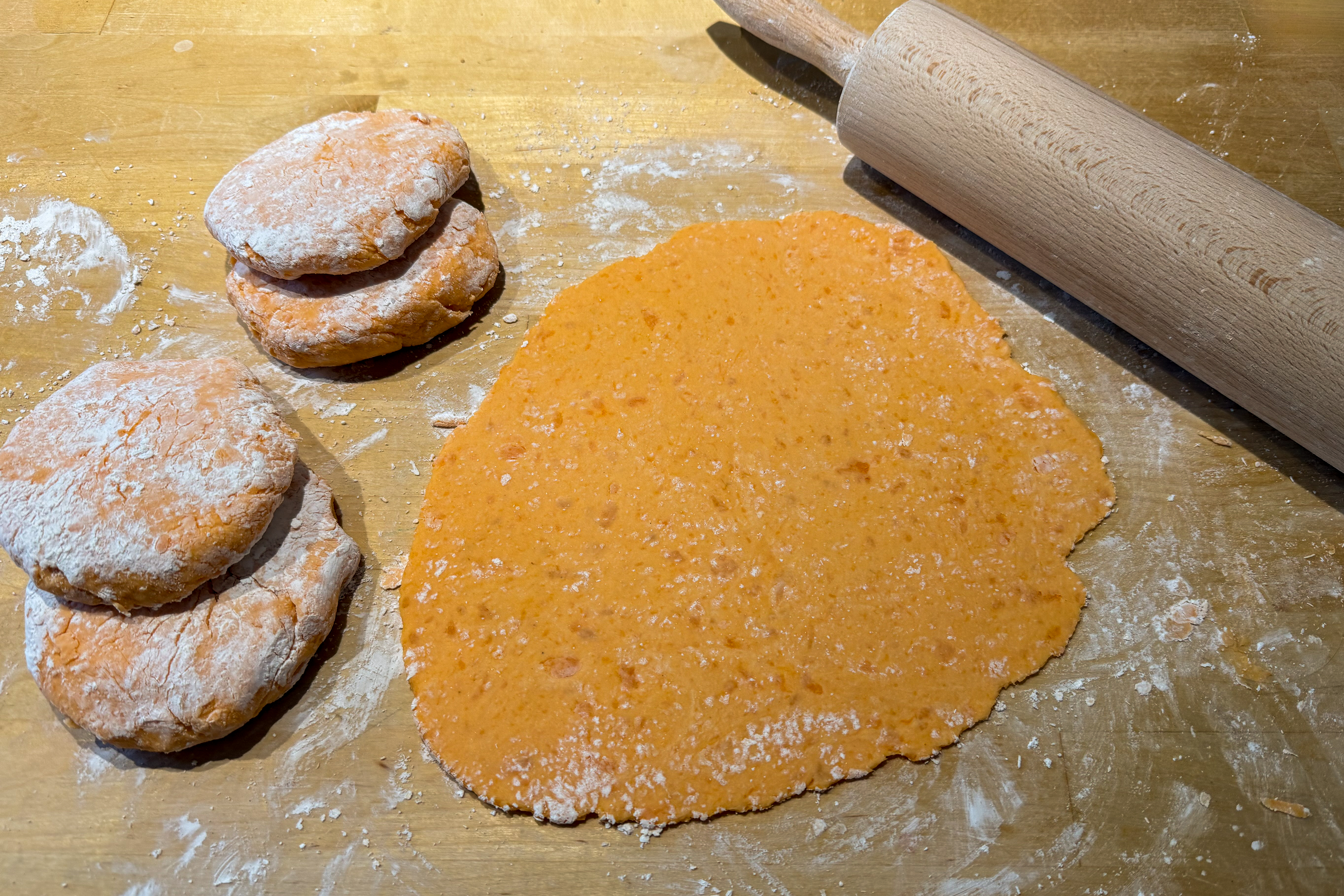 Utkavlad sötpotatisdeg till hemlagade tortillas på ett mjölat bakbord med kavel.