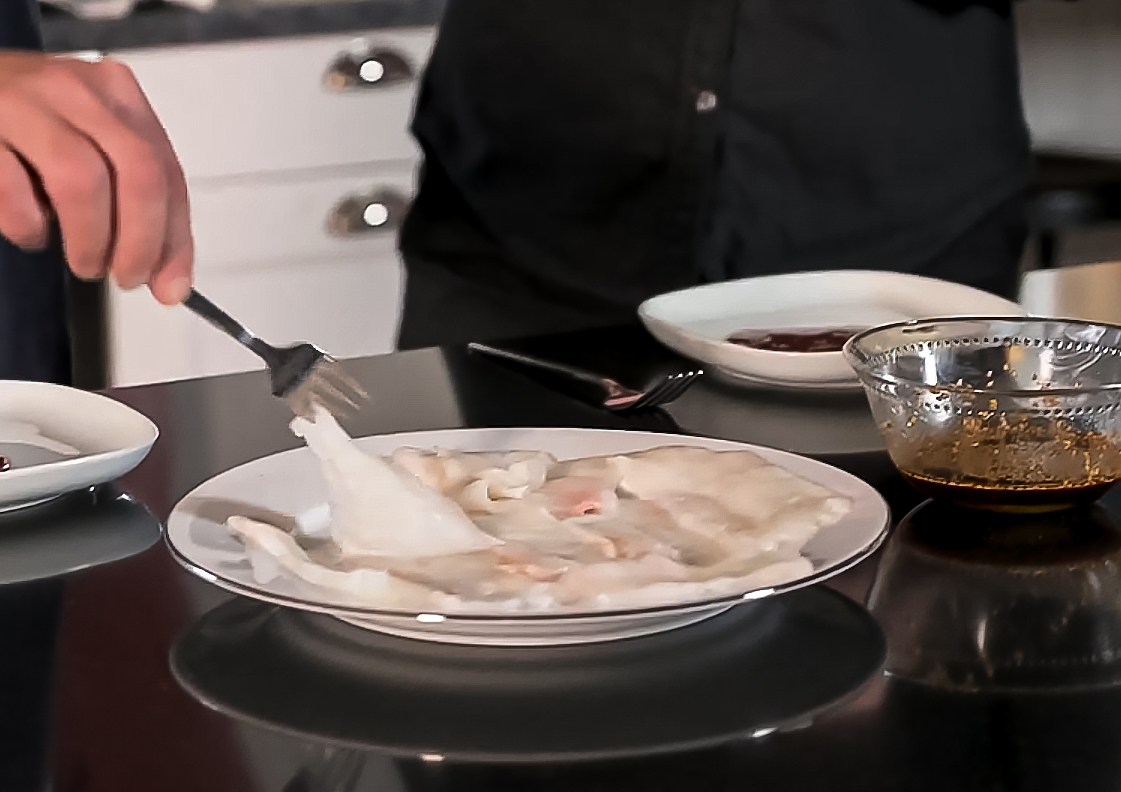 Sashimi på hälleflundra i tunna skivor på ett fat med skålar av soja och tillbehör